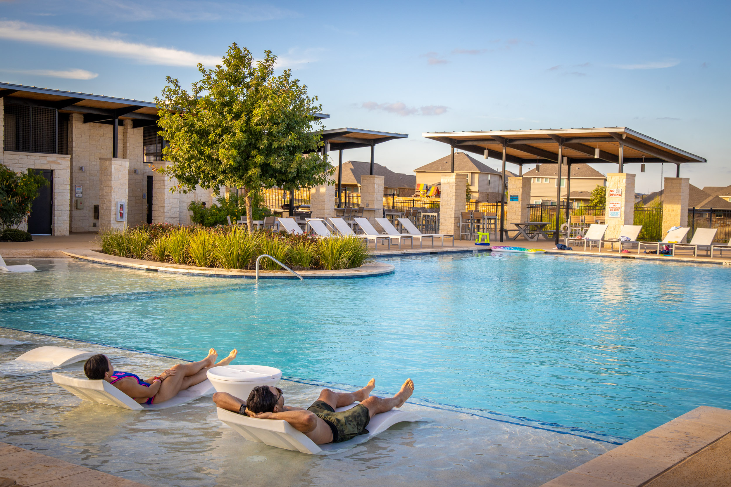 Two people lounging on deck chairs next to pool at Veramendi Ledge amenity 