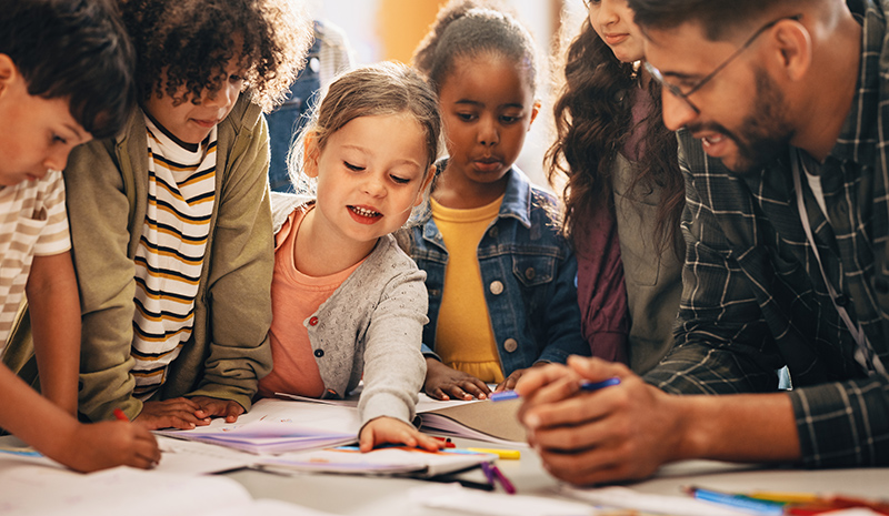 Elementary school students working on a group project while a teacher supervises 